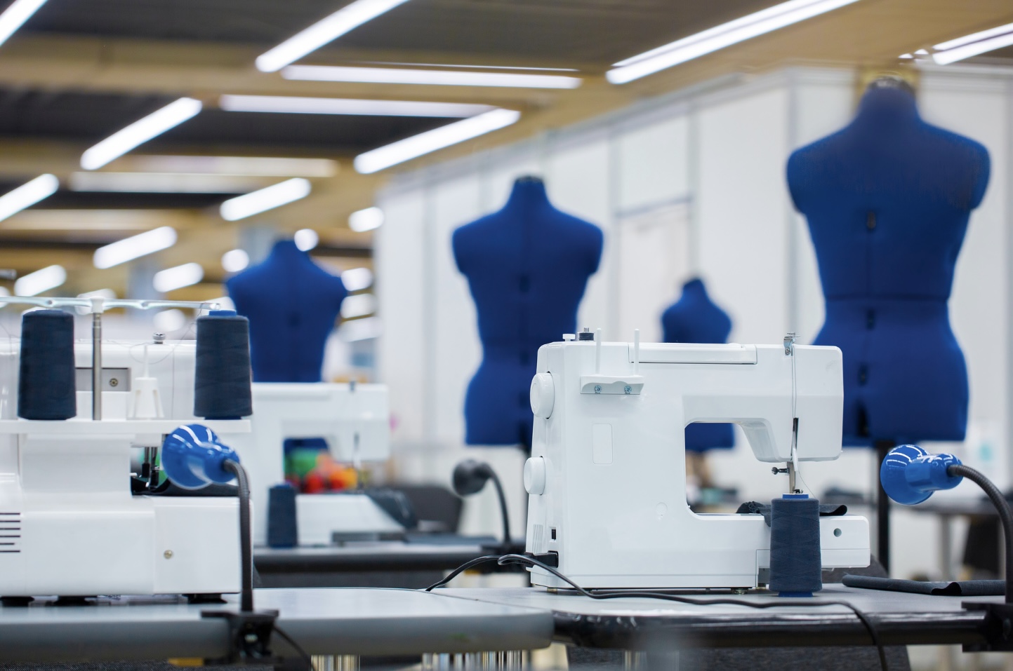 Apparel production floor with industrial sewing machines, thread cones, and dress forms in a garment factory